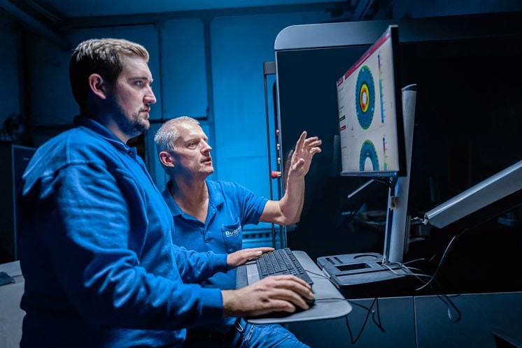 Two metrologists stand at the computer and evaluate the quality of a part in a software.